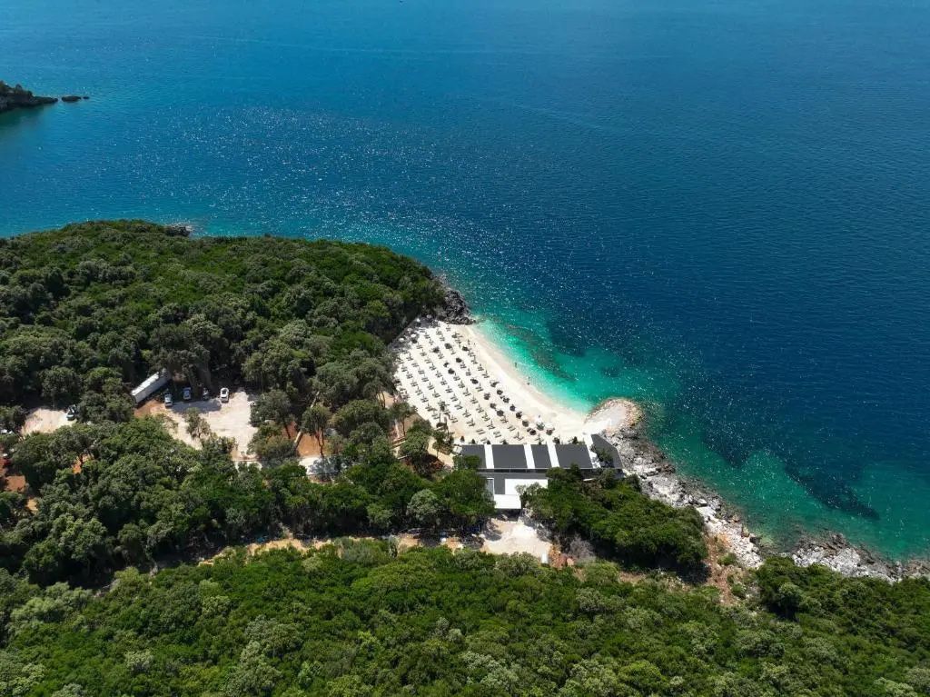 Bucht an der albanischen Riviera bei Ksamil von oben, türkisfarbenes Wasser, Strand mit Sonnenschirmen und bewaldete Landzunge