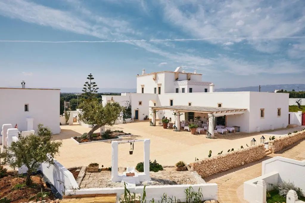 Boho Hotel in Apulien: weiß gekalkte Masseria mit Olivenbaum, Trockenmauer und Innenhof unter apulischem Himmel