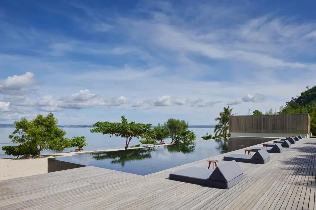 Infinity-Pool mit Blick aufs Meer und Liegen unter Bäumen im Innit Lombok