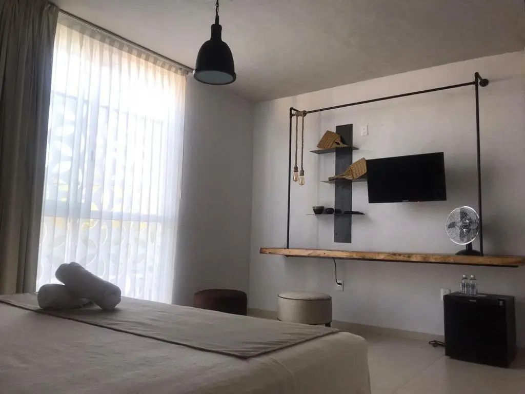 Modernes Hotelzimmer mit Fernseher an der Wand, Holzschreibtisch und hellem Vorhang.