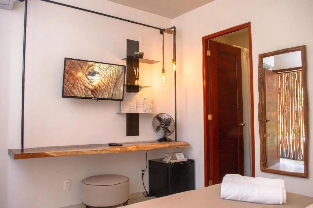 Zimmerbereich mit Fernseher an der Wand, Holzschreibtisch, Minibar und Hocker.