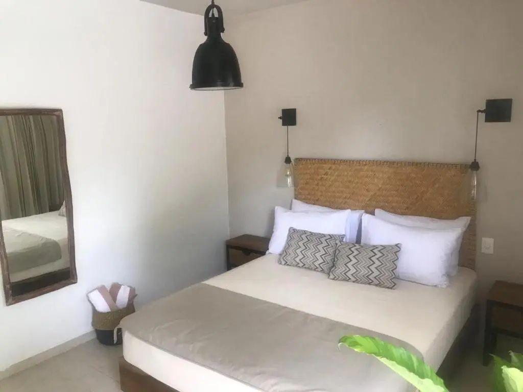 Doppelbett mit geflochtenem Kopfteil und schwarzer Hängelampe im hellen Hotelzimmer
