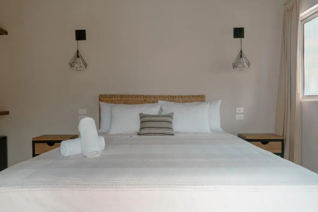 Doppelbett mit weißer Bettwäsche, gerollten Handtüchern und Drahtlampen.