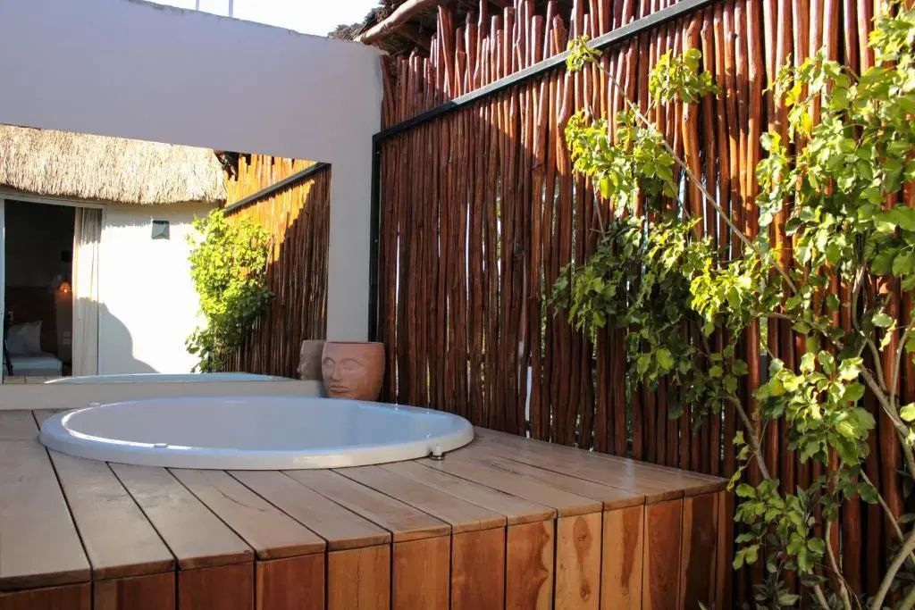 Runder Whirlpool auf einer Holzterrasse vor einer Wand aus Holzstämmen.