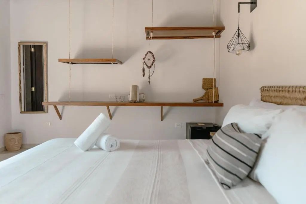 Zimmerbereich mit Bett, gerollten Handtüchern und hängenden Holzregalen.