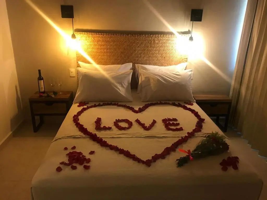 Doppelbett dekoriert mit roten Rosenblüten in Herzform im abgedunkelten Hotelzimmer