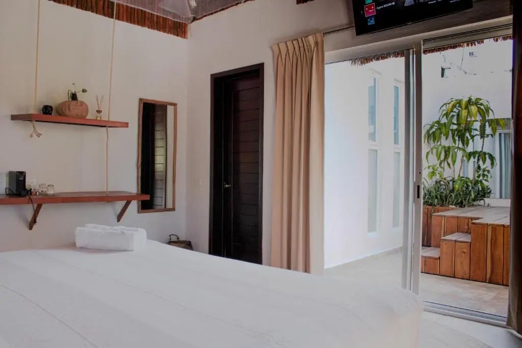 Helles Hotelzimmer mit weißem Bett, einer dunklen Tür und Schiebetür nach draußen.