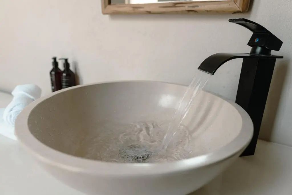 Nahaufnahme eines runden Waschbeckens mit fließendem Wasser aus schwarzem Wasserhahn.