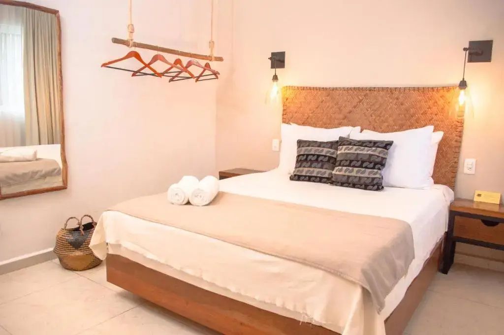 Helles Hotelzimmer mit Doppelbett, Kissen und Hängekleiderstange aus Holz.