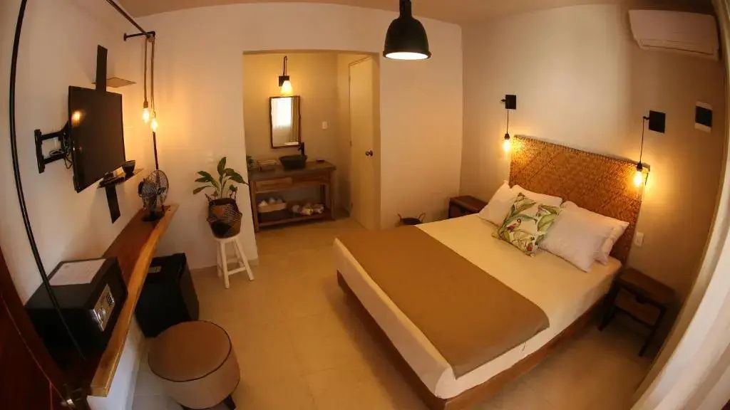 Hotelzimmer mit Holzoptik-Geflecht am Bett und Blick auf das offene Badezimmer.