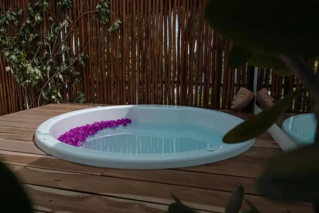 Runder Whirlpool mit pinken Blüten auf einer Holzterrasse vor Bambuszaun.