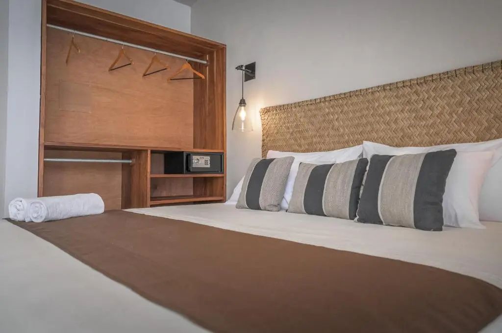 Blick auf ein Bett mit Kissen sowie einen offenen Holzschrank mit Kleiderbügeln und Safe.