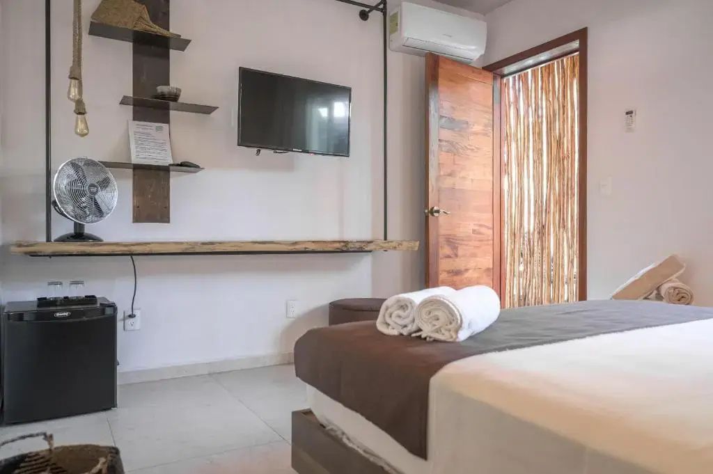 Hotelzimmer mit Wandfernseher über einer Holzablage, Klimaanlage und offener Holztür.