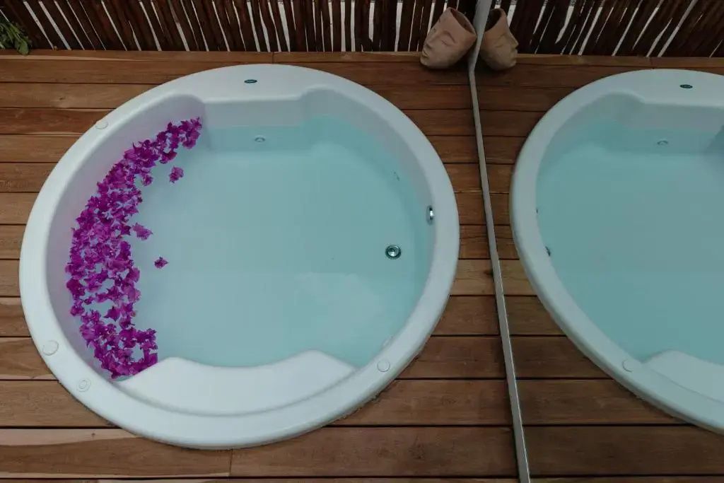 Blick von oben auf einen runden Whirlpool mit Blüten auf der Holzterrasse.