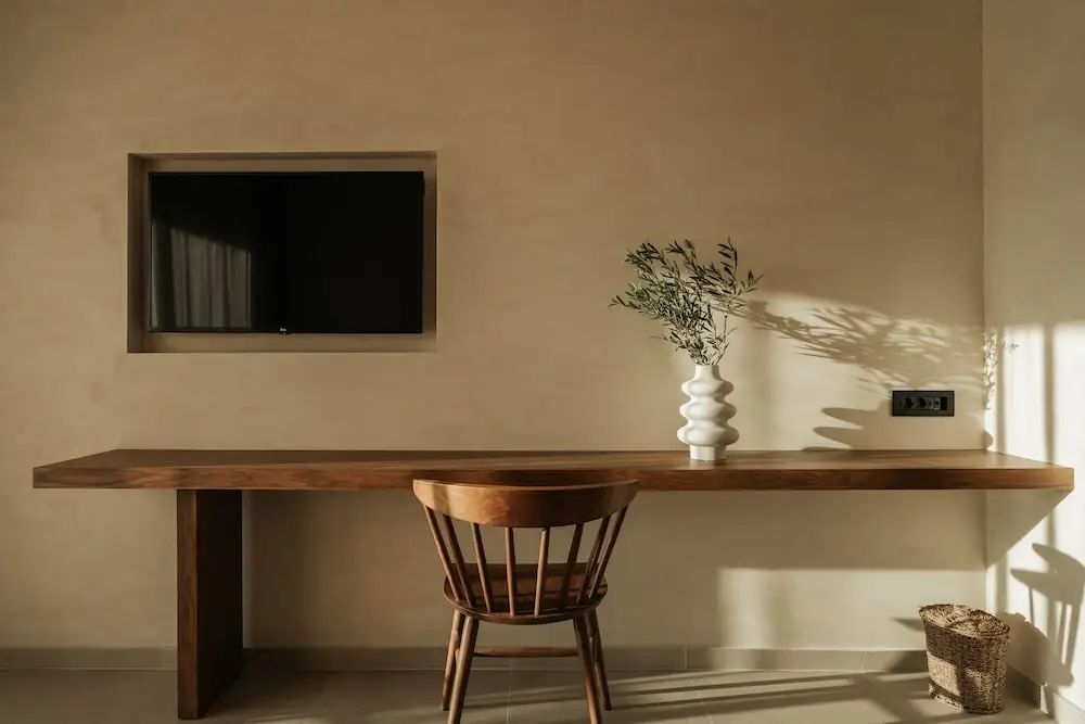 Holzschreibtisch mit Holzstuhl und Vase vor beiger Wand mit montiertem Fernseher.