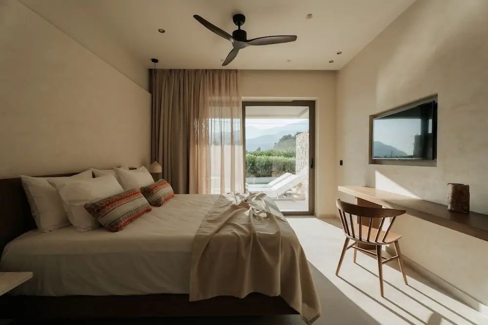 Heller Schlafraum mit Doppelbett, Deckenventilator und Schiebetür zur Terrasse mit Bergblick.