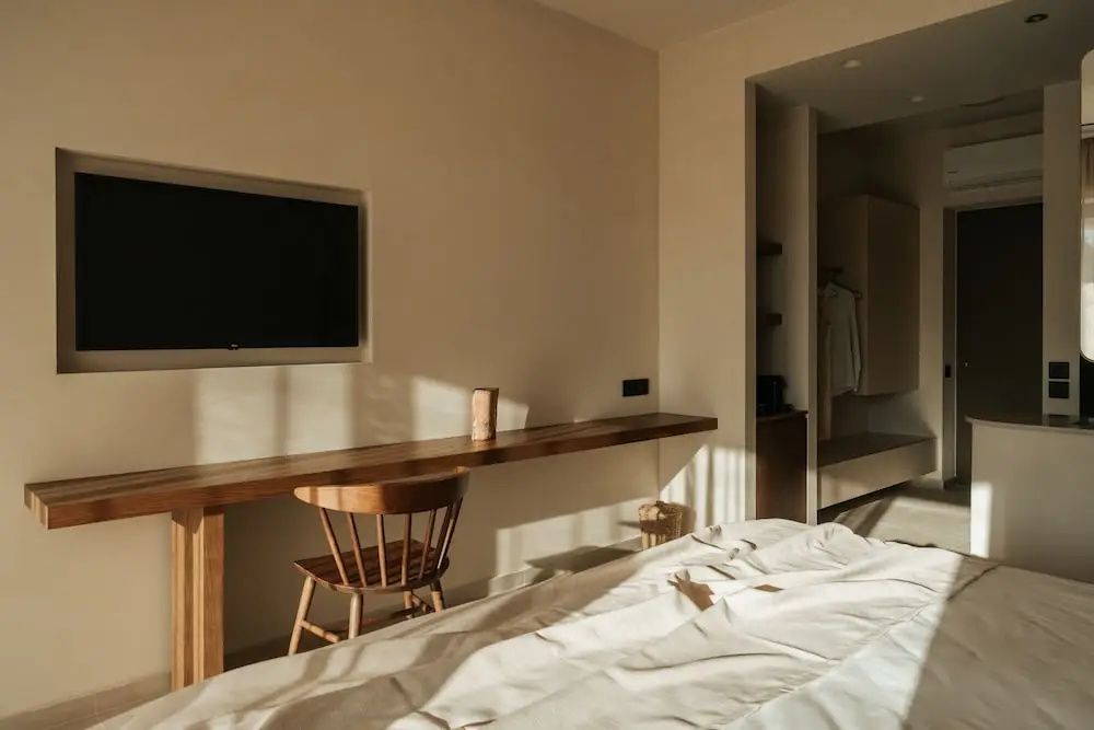 Holzschreibtisch mit Holzstuhl unter einem Flachbildfernseher an einer hellen Zimmerwand.