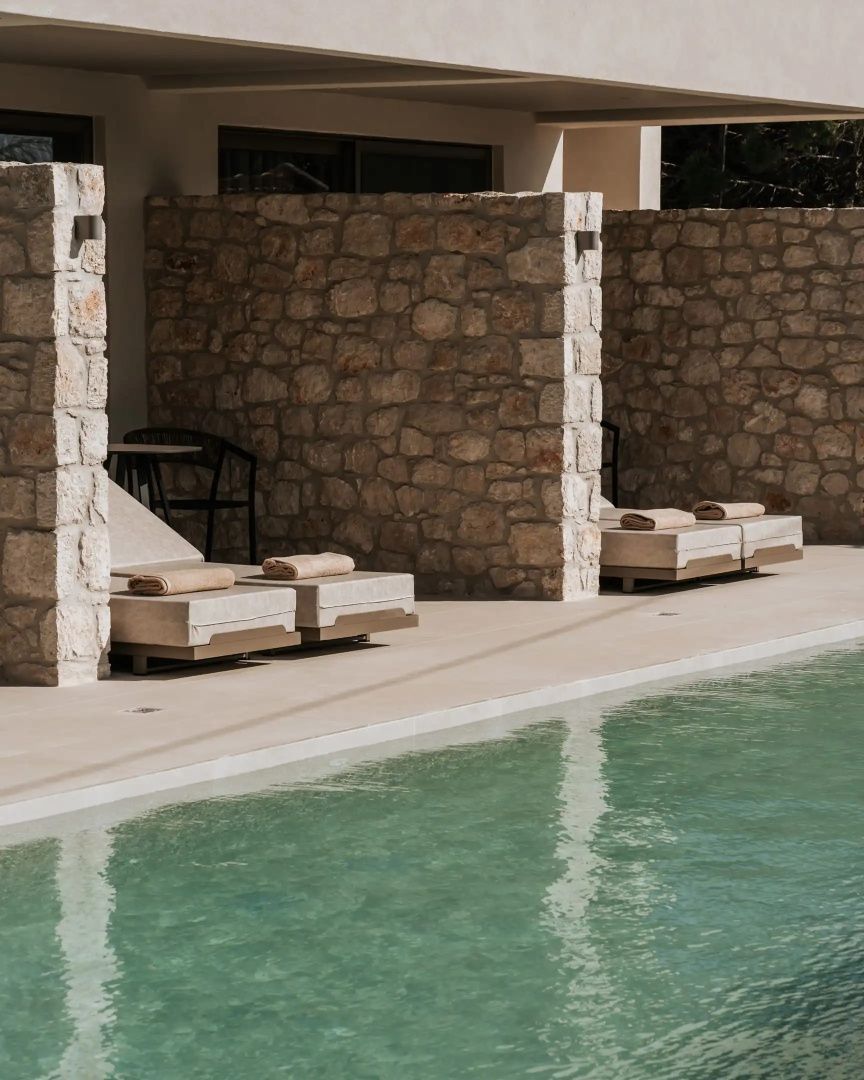 Außenbereich mit Natursteinmauern, Sonnenliegen und angrenzendem Pool.