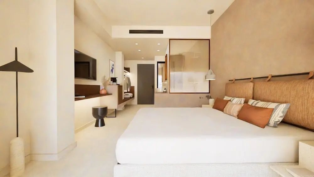 Helles Hotelzimmer mit Doppelbett Wandfernseher und Blick in den angrenzenden Badbereich.