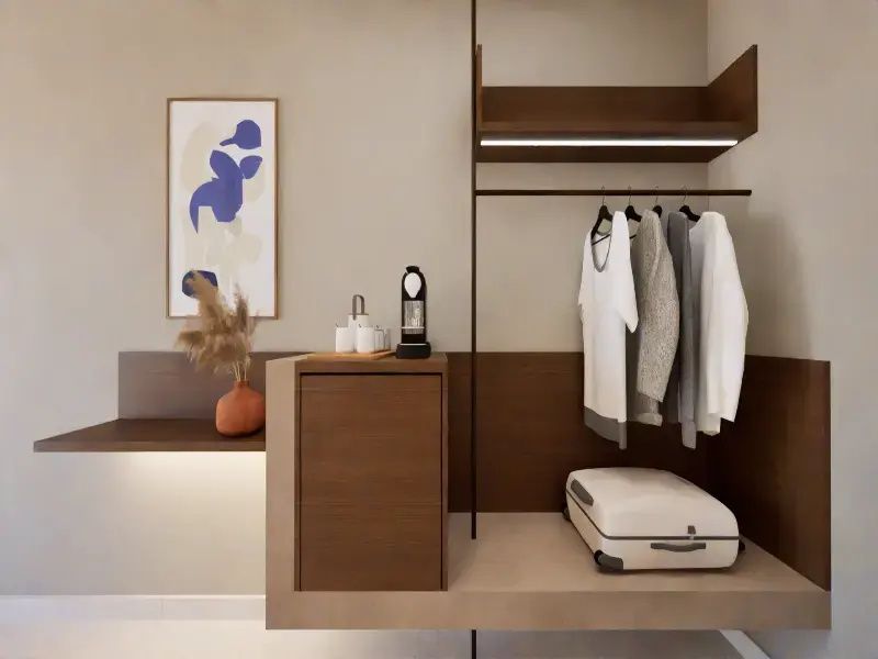 Offener Kleiderschrankbereich im Hotelzimmer mit aufgehängter Kleidung und Koffer.