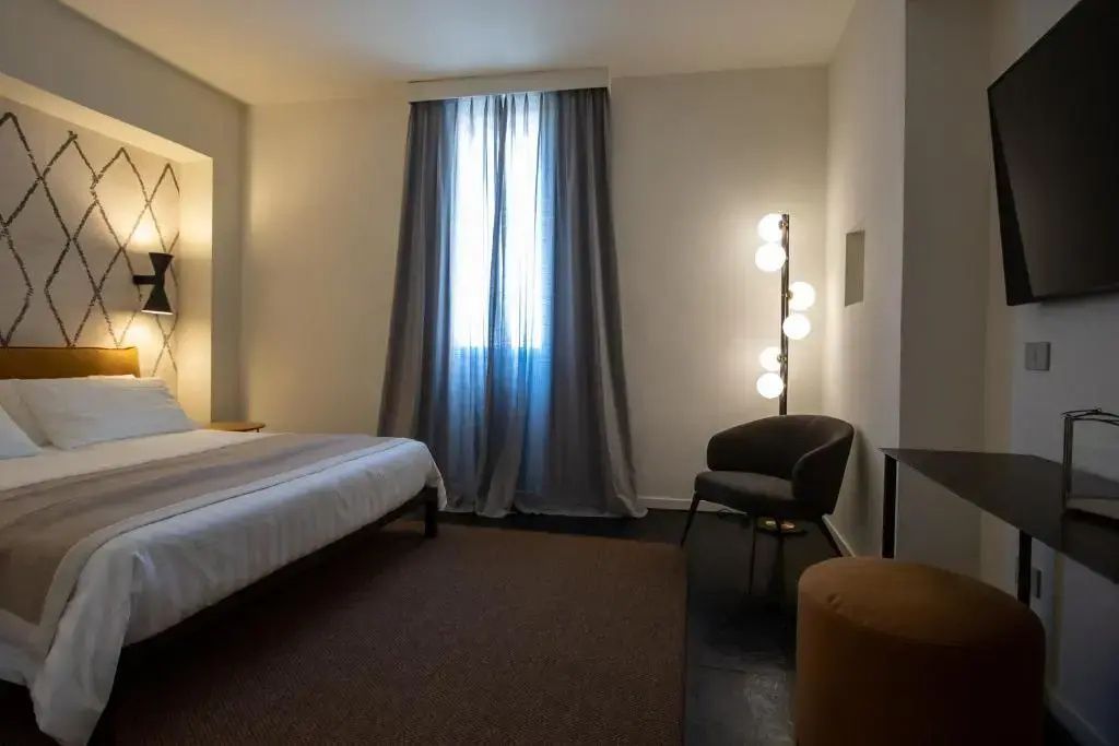 Modernes Hotelzimmer mit Doppelbett, Stehleuchte, einem Sessel und langen Vorhängen.