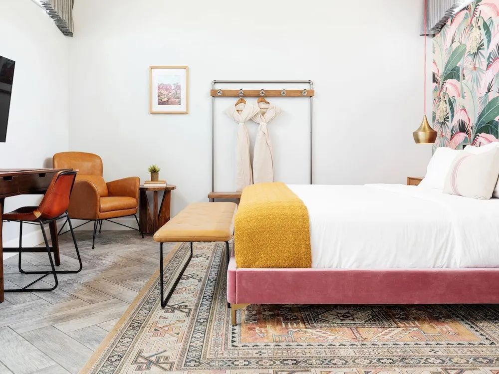 Doppelbett mit rosa Rahmen, gelber Decke, Ledersessel und Kleiderständer im Zimmer.