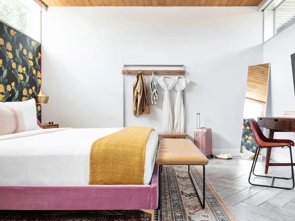 Schlafzimmer mit Doppelbett, gepolsterter Sitzbank, Kleiderständer und Koffer.