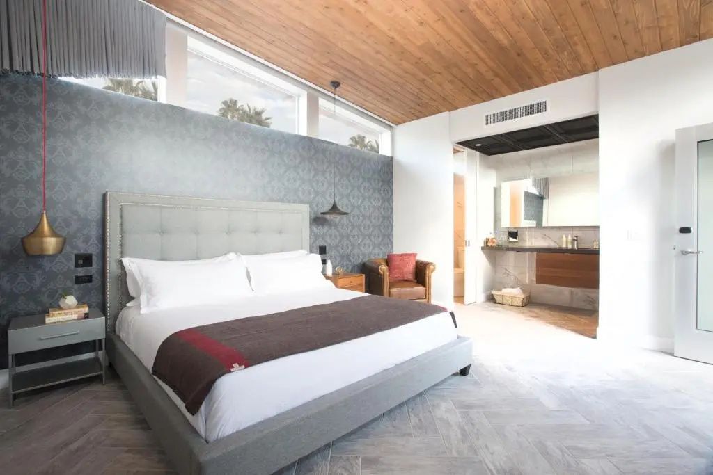 Helles Zimmer mit großem Doppelbett, hoher Holzdecke und angrenzendem Waschtisch.