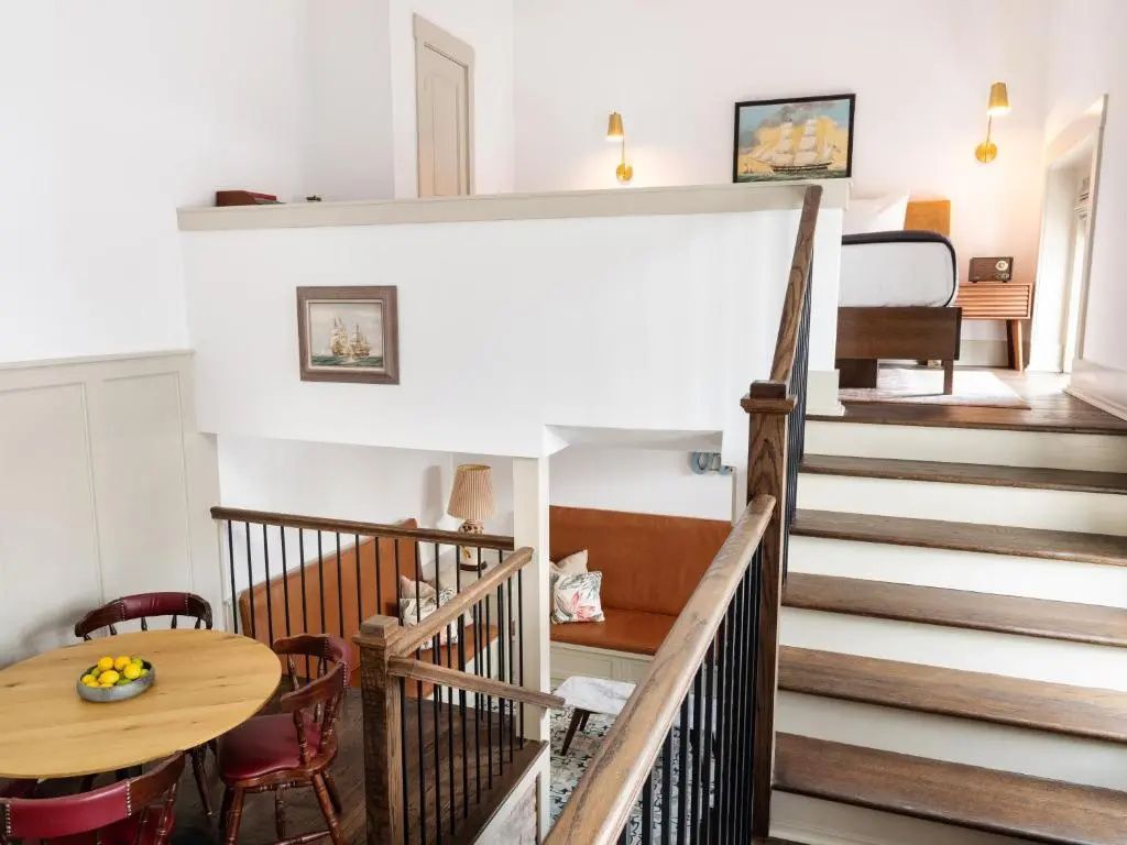 Zweigeschossiges Zimmer mit Holztreppe, Sitzbereich unten und Schlafbereich oben.