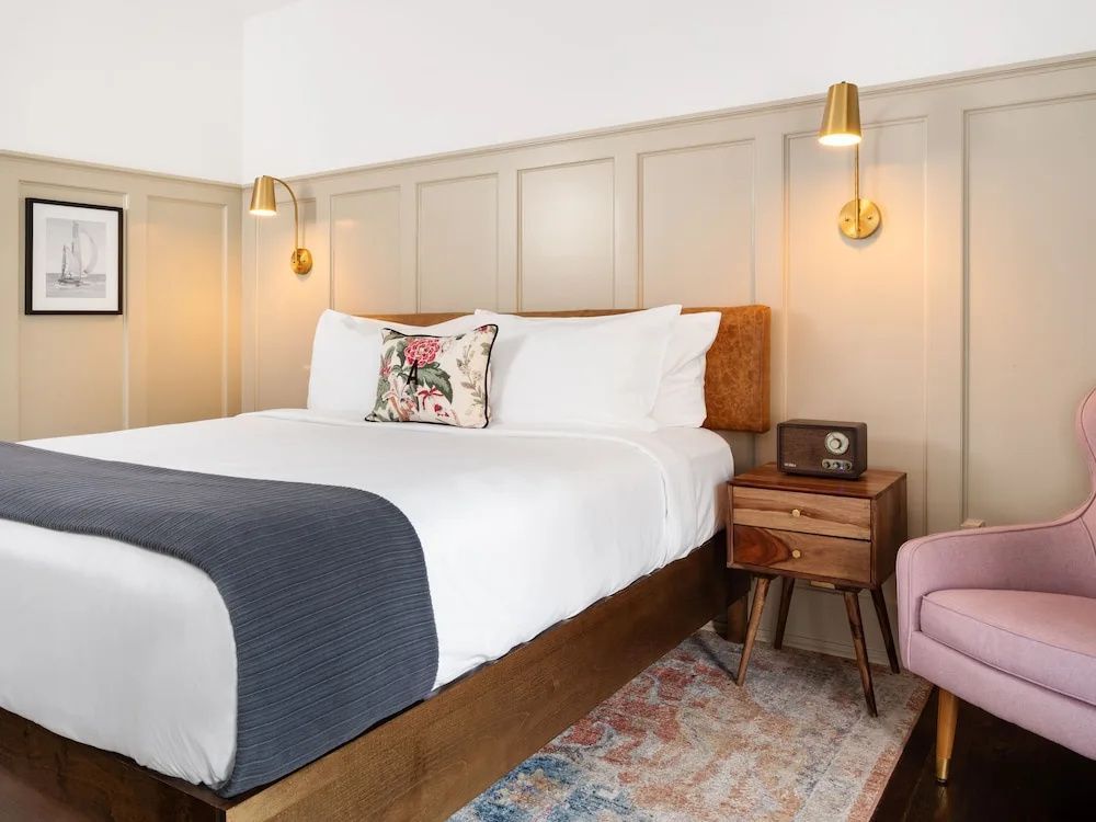 Doppelbett im Hotelzimmer neben einem Holznachttisch mit einem Radio im Retrodesign.