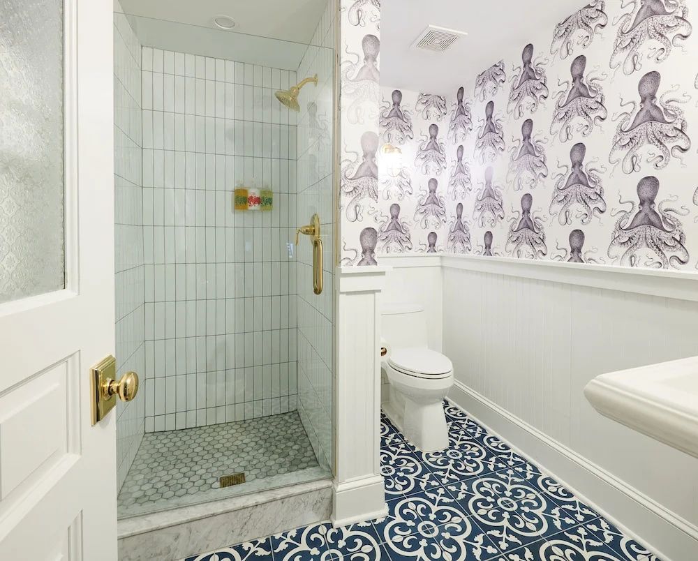 Badezimmer mit bodentiefer Dusche, Oktopustapete und blau gemusterten Bodenfliesen.