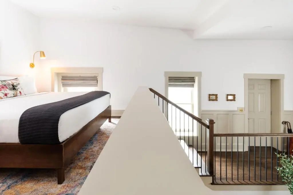 Loft-Schlafbereich mit großem Bett, buntem Teppich und Holztreppe nach unten.