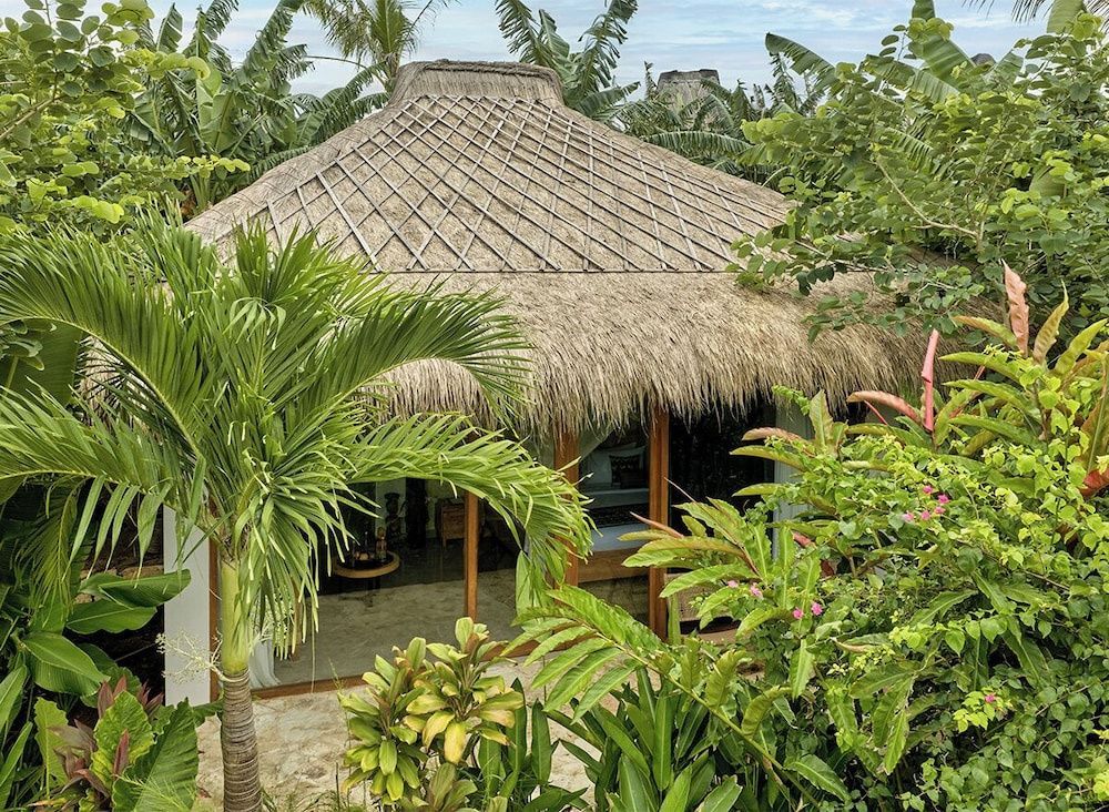 Traditioneller Bungalow mit Strohdach inmitten tropischer Pflanzen und Palmen.