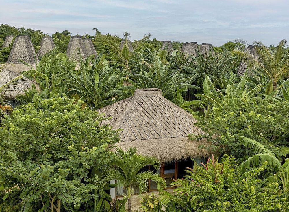 Traditionelle Bungalows mit Strohdächern inmitten von tropischen Pflanzen und Palmen.