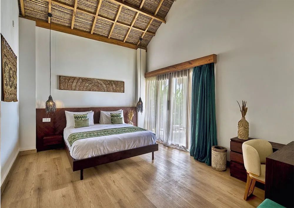 Schlafzimmer mit Doppelbett, Holzfußboden, grünen Akzenten und hoher Reetdachdecke.