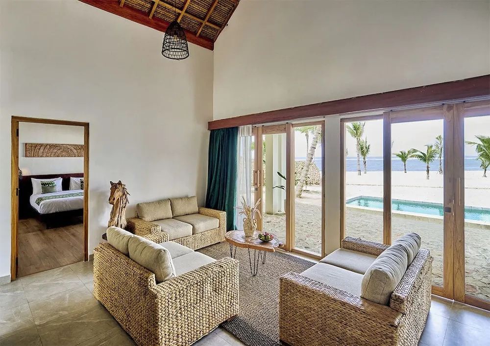Wohnbereich mit Rattan-Sofas und Blick durch große Glasfenster auf einen Pool und das Meer.