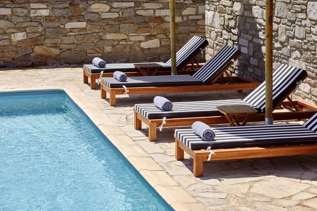 Holzsonnenliegen mit gestreiften Auflagen stehen neben einem Pool an einer Natursteinmauer.