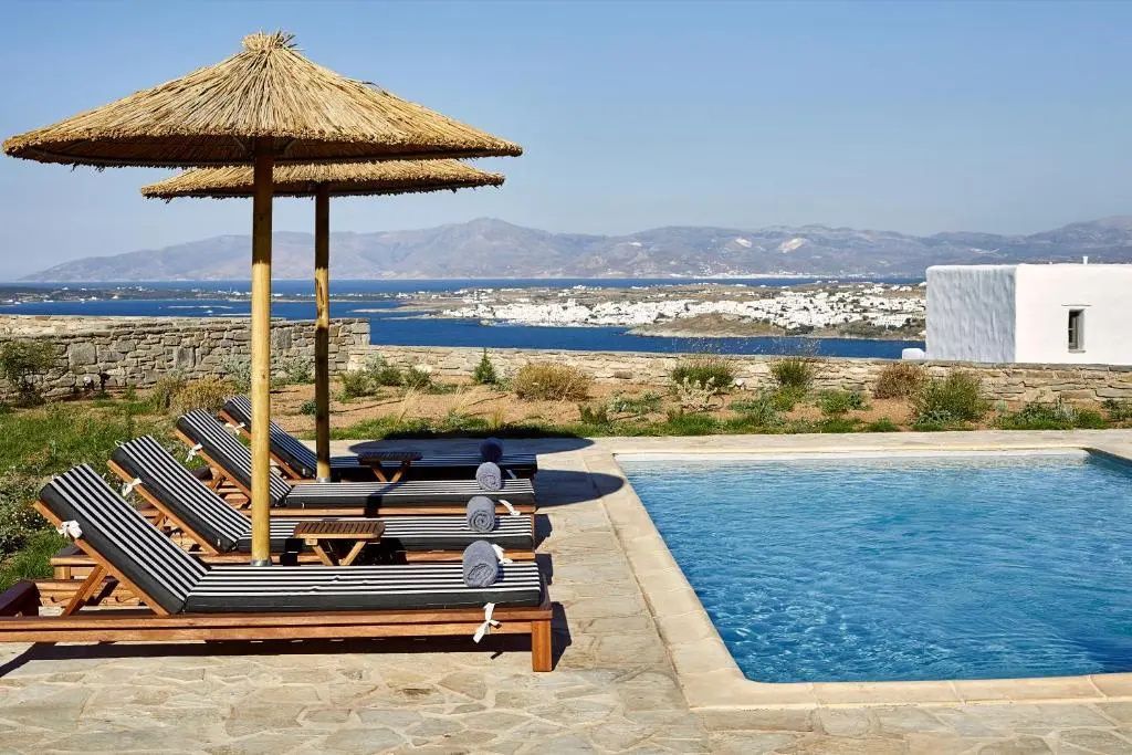 Terrasse mit Pool, Sonnenliegen und Sonnenschirmen sowie Weitblick auf das Meer und die Küste.