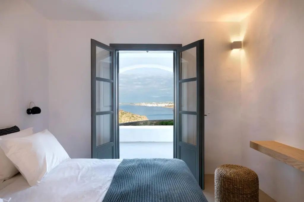 Blick aus dem Schlafzimmer durch geöffnete Flügeltüren auf die Küste und das Meer.