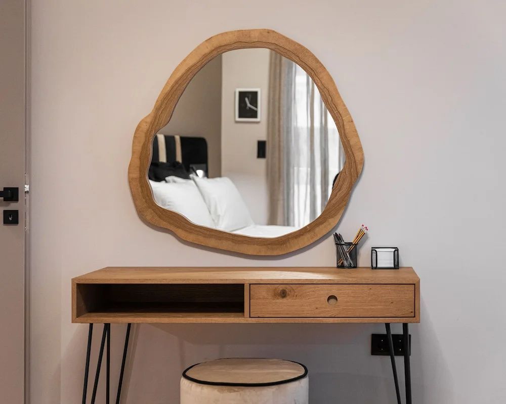 Schreibtisch aus Holz mit einem organisch geformten Wandspiegel und einem Hocker.