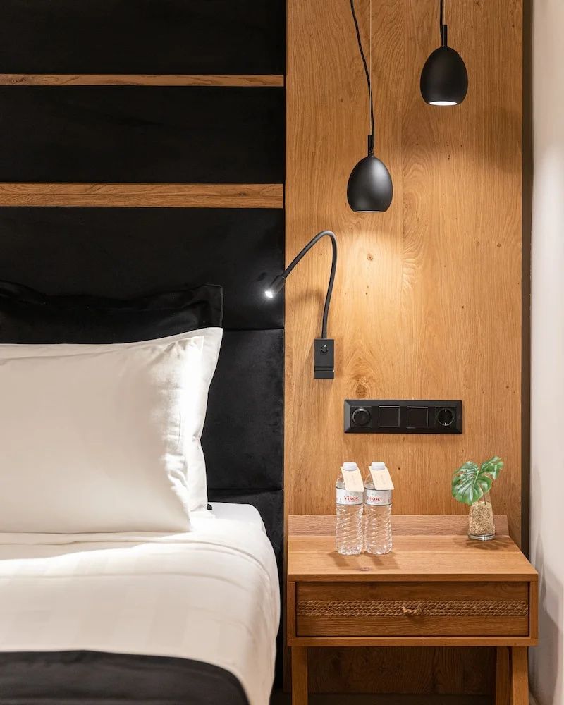 Nachttisch aus Holz mit zwei Wasserflaschen neben einem Bett mit schwarzem Kopfteil.