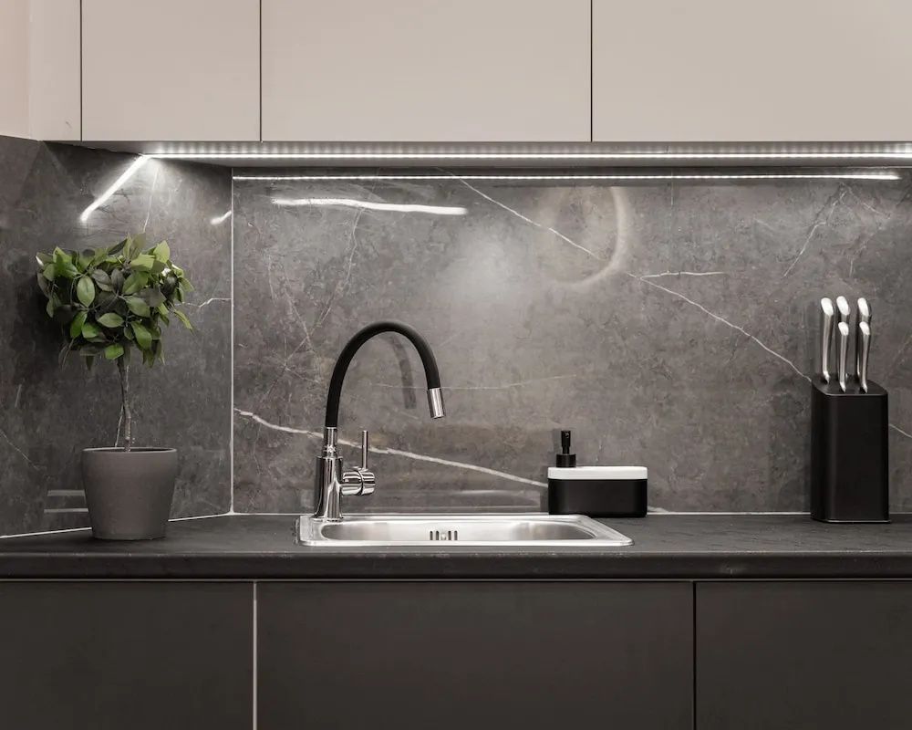 Moderne Küchenzeile mit Spülbecken, schwarzem Wasserhahn und dunkler Rückwand.