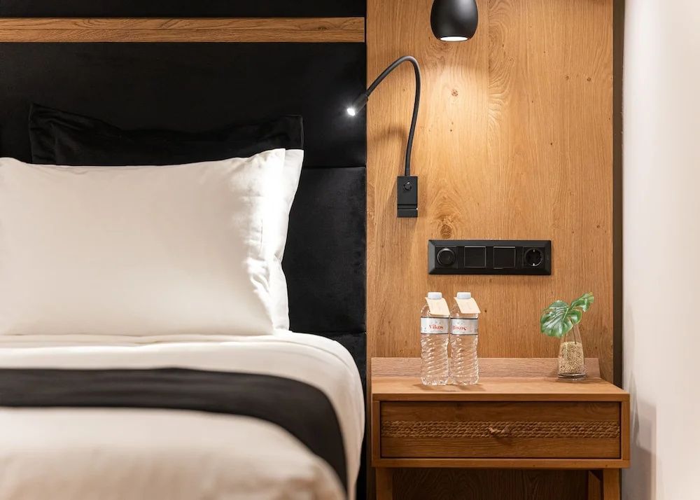 Holznachttisch mit Wasserflaschen und Leselampe neben weiß belegtem Bett.
