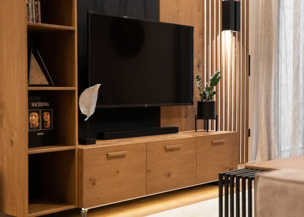 Flachbildfernseher an der Wand über einem niedrigen Holzschrank mit Zimmerpflanze und Dekoration.