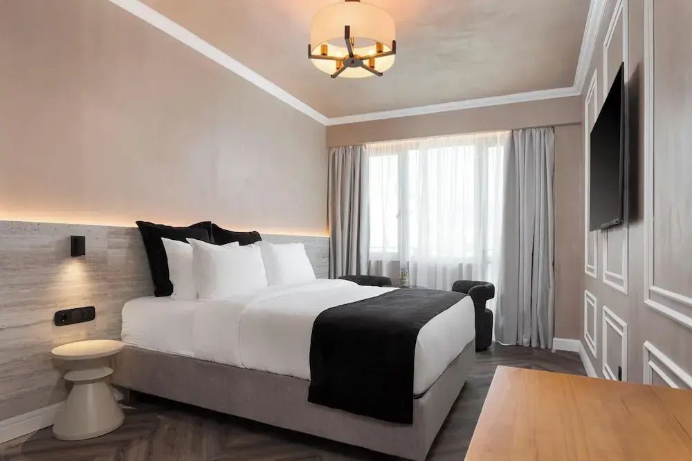 Helles Schlafzimmer mit großem Doppelbett, Fensterelement und Vorhängen.