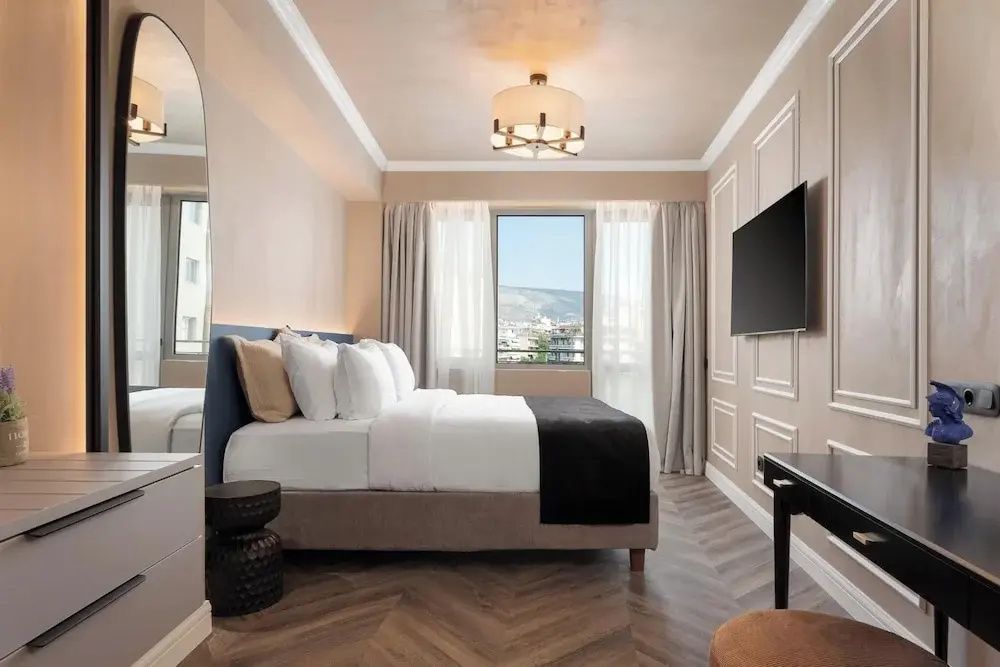 Geräumiges Schlafzimmer mit Doppelbett, Wand-TV und Blick auf die Stadt durch das Fenster.
