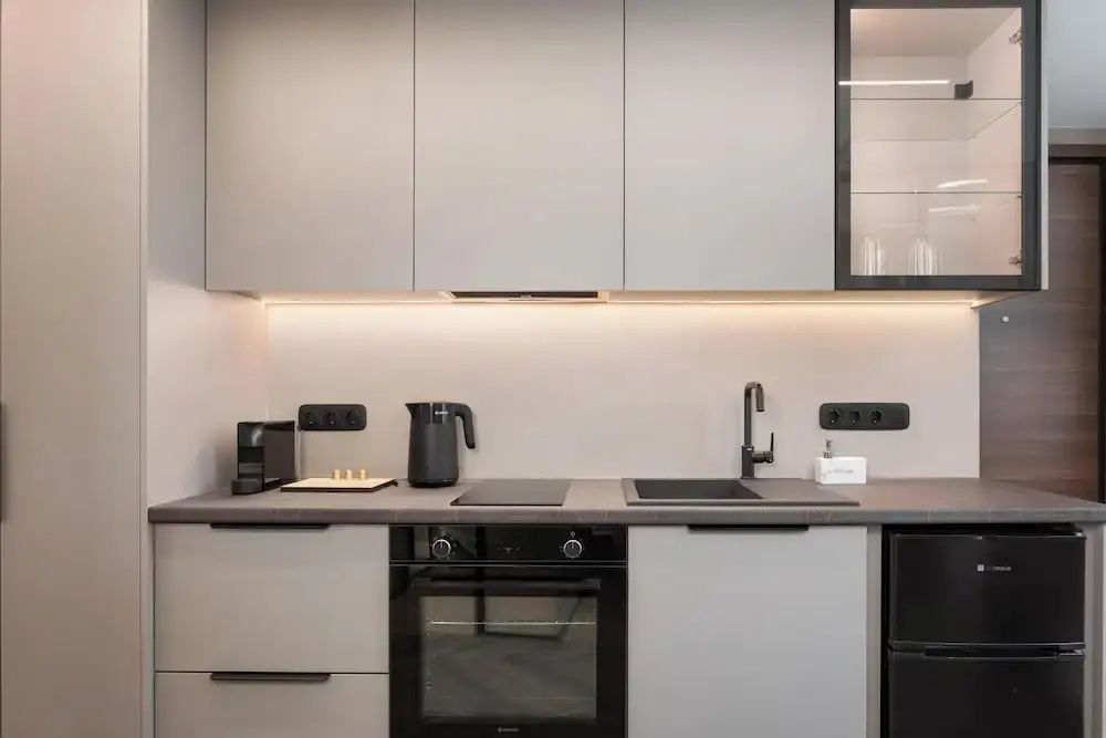 Moderne Küchenzeile mit Herd, Backofen, Spülbecken und Hängeschränken mit Licht.