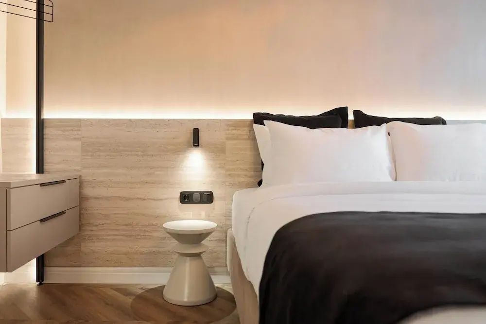 Modernes Bett mit beleuchteter Wand und kleinem runden Beistelltisch im Zimmer.