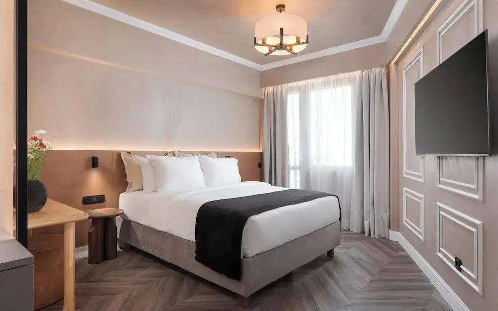 Schlafzimmer mit Doppelbett, weißer Bettwäsche, Holzfußboden und hellen Vorhängen.