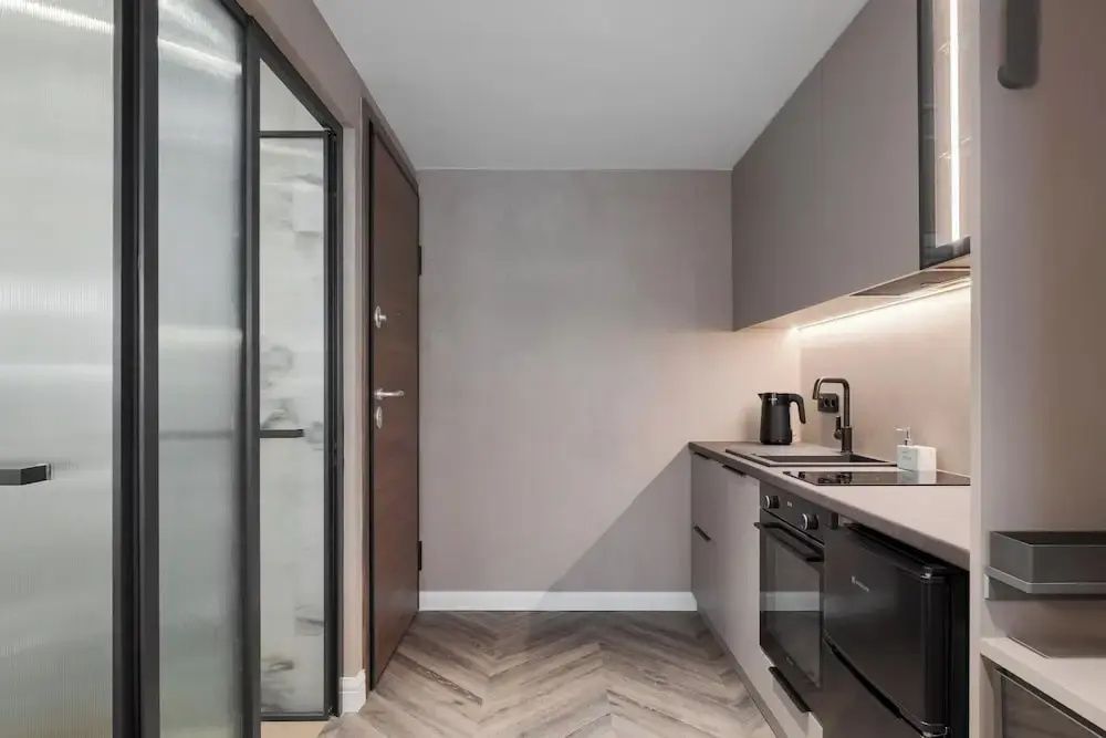 Moderne Küchenzeile in der Suite mit Kochfeld, Spüle, dunklen Schränken und Parkettboden.